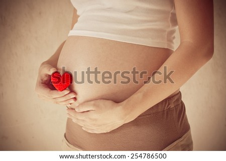 Pregnant woman holding her hand on belly And holding a red heart, Vintage filter