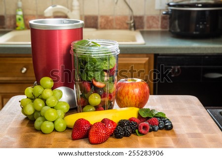 Healthy fruits with small blender on a cutting board getting ready for making a smoothie in a kitchen setting.