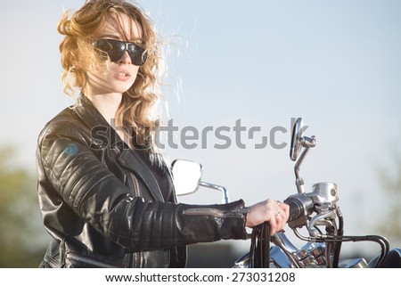 Biker girl in the  leather jacket on a motorcycle looking at the sunset.