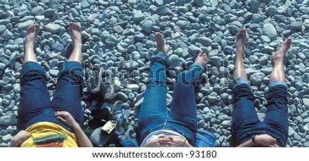3 barefooted girls sunbathing on a stone covered beach.