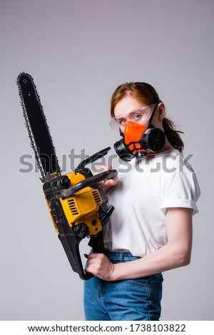 Red-haired girl in white T-shirt in construction respirator and goggles holds a chainsaw. Advertising banner for a hardware store. Stock fotó © 