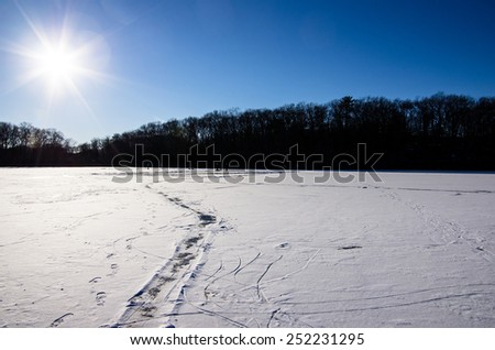 A frozen pond covered in snow, has a path cleared through the snow.