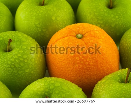 Green apples and one Orange arranged as a full frame background all wet with mist.