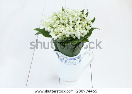 Beautiful bouquet of lilies of the valley in white jug on white painted wooden table