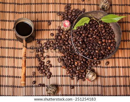 Vintage turkish coffee pot and coffee beans in old silver plate with leafs on brown bamboo mat with packed chinese Pu-Ehr tea. View from the top.