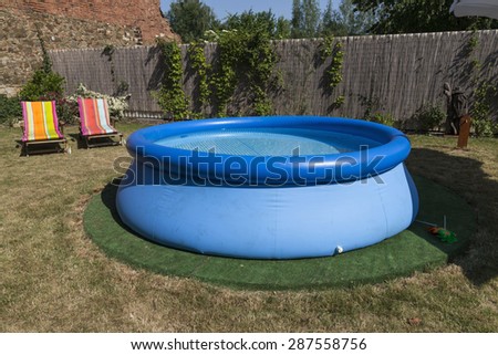 blue rubber pool on the grass for children, 2 lawn chairs in the back