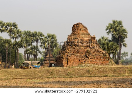 Inwa (Ava) - Ruins of brick temple, resting Burmese man and two typical colorful carts.