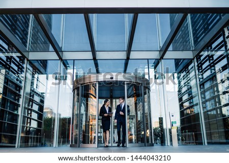 Formal contemporary man and woman talking while walking out of round revolving doors of modern glass building of corporation office  Foto d'archivio © 