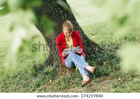 Young woman in office dress code with digital tablet under the tree in a park.