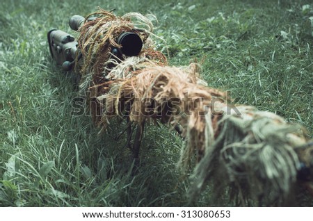 Camouflaged sniper rifle with spotting scope and equipment. Photo edited into warfare look and dark atmosphere. Selective focus.
