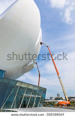 Marina Bay Sand, Singapore - May 9, 2015 : Worker is painting the outside of ArtScience Museum, Singapore by standing in basket of articulating boom lift.
