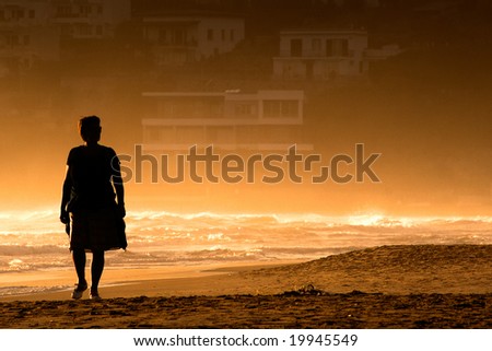 A silhouette of a woman walking along the sea-shore with a stormy sea in the sunset