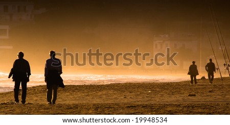 Two couples of silhouettes of men walking along a misty and orange seashore