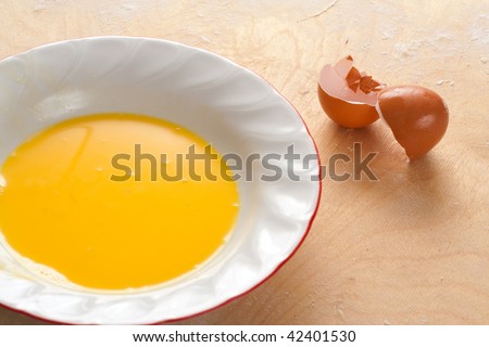 A plate with beaten egg yolks and a broken egg shell on a wooden and floured board
