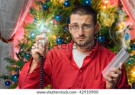 An handsome man showing a broken plug of Christmas Tree lights exploding and causing the burnt of an Hard Disk. The concept of frustration and sadness.