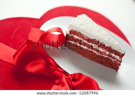 A plate with a slice of rich red velvet cake with cream cheese filling and coconut icing. Shallow depth of field on cake tip and ribbon