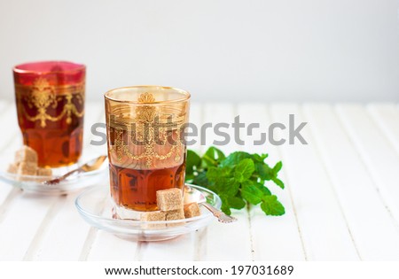 Moroccan tea with mint and sugar in a glass on a white table with a kettle