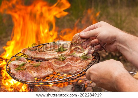 Men\'s hands hold the grille with meat on fire background