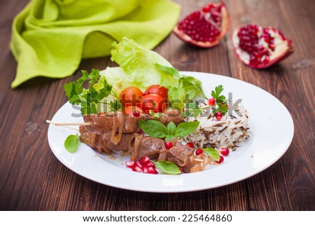 kebab and wild rice with a salad of fresh vegetables and pomegranate seeds on a white plate