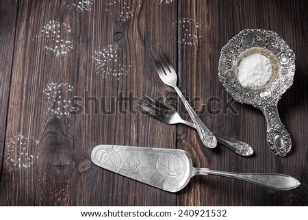 silver cutlery for dessert - strainer for powdered sugar, cake spatula and forks on a wooden background