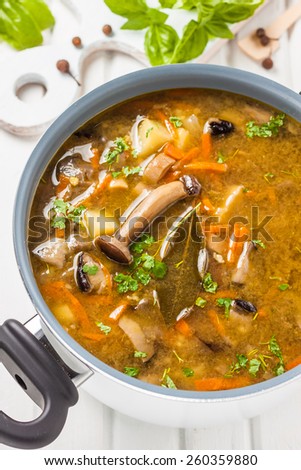 mushroom soup with carrots, millet and potatoes in a white pot on a light wooden background