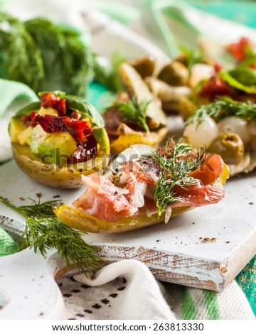 potatoes stuffed with vegetables. Boats potatoes with avocado, sun-dried tomatoes, bacon, cheese, olives, pickled cucumbers and greens on the board on a green wooden background. Picnic, barbecue grill