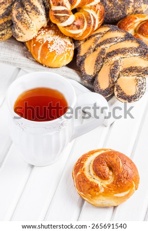 Cup of tea with sweet buns.Fresh white bread rolls on a tray on a white wooden background.Â  Buns with poppy seeds, sesame seeds and sugar for breakfast
