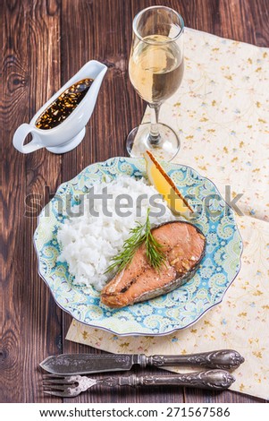 Baked salmon with rice garnish. Plate with grilled salmon, rice, lemon and a glass of wine on the table. Lunch / dinner.