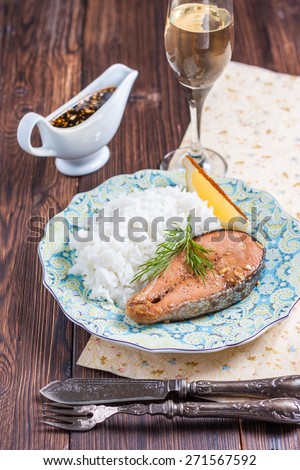 Baked salmon with rice garnish. Plate with grilled salmon, rice, lemon and a glass of wine on the table. Lunch / dinner.