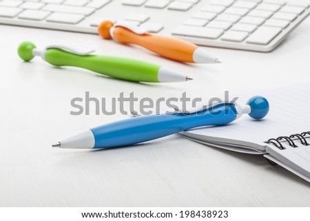 Blue, green and orange plastic ball pens at the back keyboard on white background.