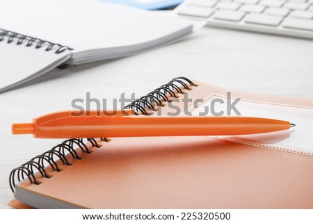 Orange ball pen with notebooks on white desk.