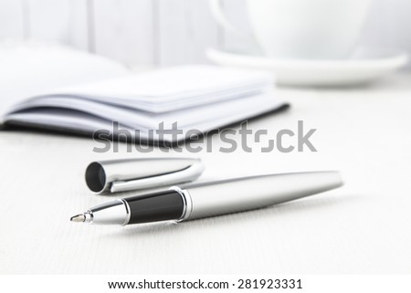 silver roller pen with notebook and coffee cup on white background