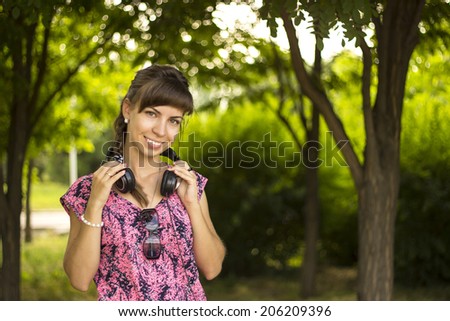 Woman listening to music. Female student girl outside in park listening to music on headphones while studying. Happy young university student of mixed European and Caucasian ethnicity.
