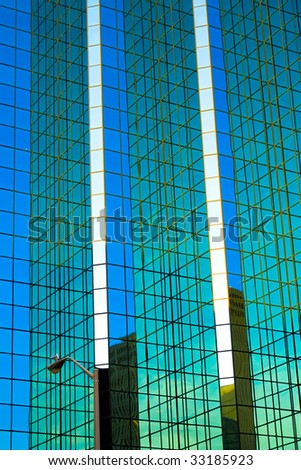 A seagull sits on a street light, dwarfed by the enormous facade of a glass skyscraper