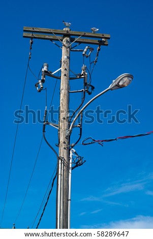 A convoluted mess of wires and cables clutter a wooden telephone pole and street lamp.