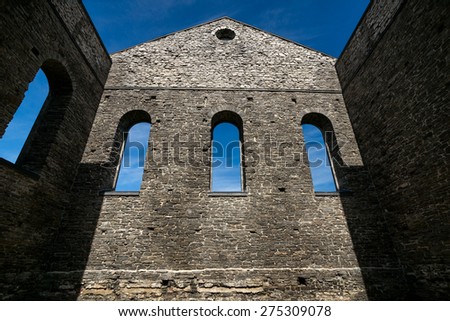 Looking up at the towering stone wall of an ancient church ruins with three gothic windows.