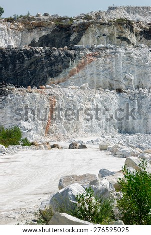The white, chalky rock of a three tiered layered cliff at an open-pit marble mine.