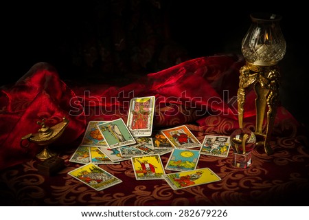 A pile of tarot cards lie scattered and spread across a table top surrounded by multiple occult items.