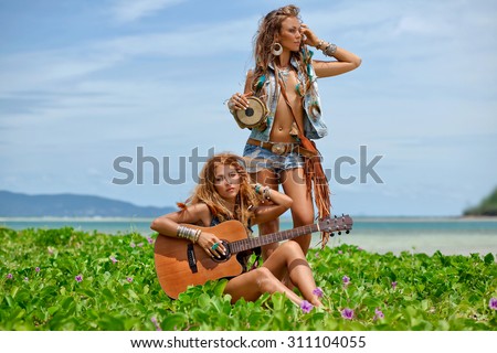 two beautiful hippie girls friends with guitar and drum on the beach