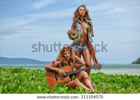 two stylish hippie girls friends with guitar and drum on the beach
