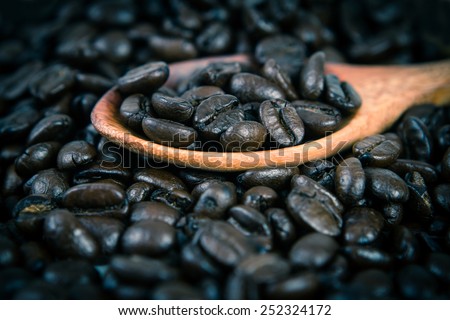 roasted coffee beans in wooden spoon placed on coffee beans as background , selective focus