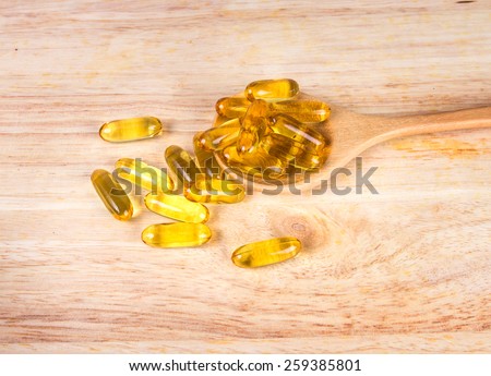 Closeup the yellow soft gelatin supplement fish oil capsule on wooden plate