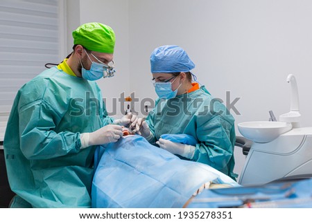 Team of dental surgeons performs surgery on teeth. in a modern clinic. Young dentist. Teamwork. Tooth doctor orthodontist surgeon doing medical operation on root canals. Stomatology office.  Stockfoto © 