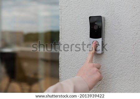 woman's hand uses a doorbell on the wall of the house with a surveillance camera