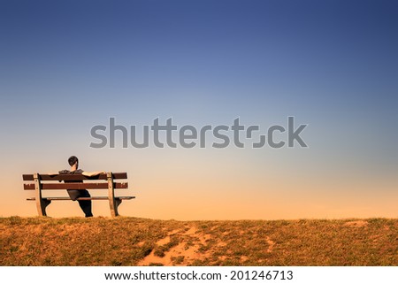 young man resting alone on a bench in an empty landscape at dusk