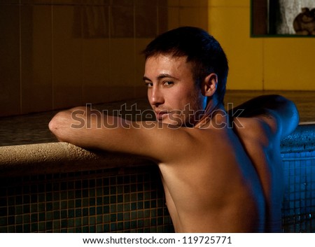 Young wet sexy muscular man posing in the swimming pool