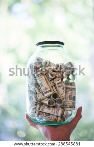 Hand holds a glass jar full of money on blurred background