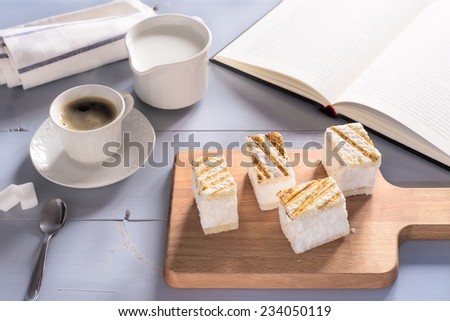 Wooden blue table with opened book, a cup of hot coffee, milk and sweets on wood tray. Relaxing time with literature, hot beverage and desserts