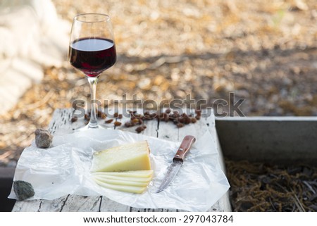 Pieces of cheese and raisins with a red wine glass on a old wooden board in the countryside. A rustic lunch with Idiazabal cheese cut and wine