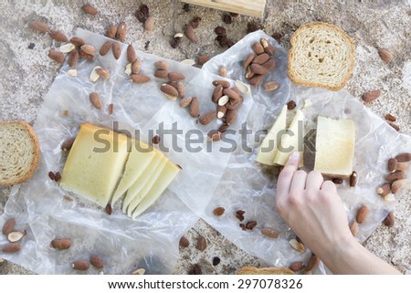 Woman hand holding a piece of cheese of snack of cheese, roasted almonds and toast. Rustic lunch of brown on stone table in the countryside